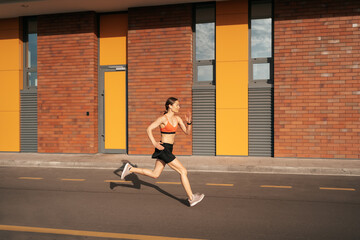 Young woman sprinting in the morning outdoors. Side view of female runner working out in the city.