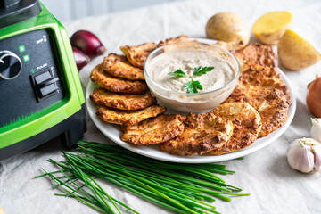 .Potato pancakes, golden, on a white plate. Garlic sauce, fresh herbs, with ingredients. Blender.