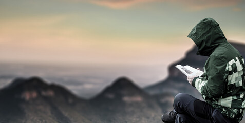 man is reading a book on a top of mountain sunset landscape.