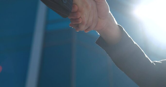 Closeup part of human body two men shake hands, conclude successful contract agreement, sign of support for partnership cooperation, businessmen in black jackets greet on street with male arms gesture
