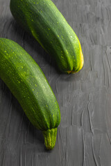 Two fresh green courgettes lie against a black background