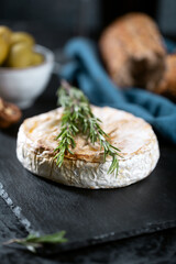 Camembert cheese with rosemary, olives and rustic bread on a dark background