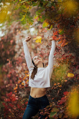 Beautiful young woman walking in autumn park.  Freedom ideas concept, woman with raised hands up in a colorful autumn park.