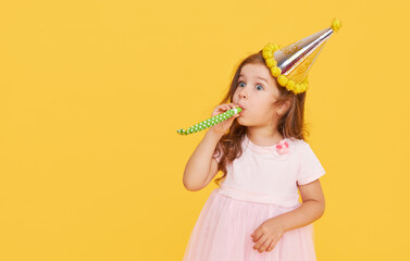 Party time. A joyful little girl in a festive cap and elegant dress celebrates her birthday....