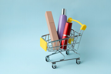 Lipstick, Foundation, and mascara in a shopping cart on a blue background. Selective focus. Sale of cosmetics. © Tatyana