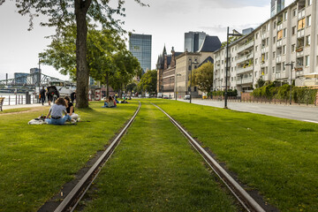 Frankfurt / Main, Germany - August 05th 2019: Visiting the river front of Frankfurt / Main at a  cloudy day in summer, view along a meadow with people sitting on it next to the so called R&ouml;merberg.