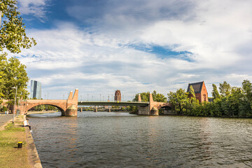 Frankfurt / Main, Germany - September 03rd 2020: A german photographer walking along the river Main during a sunny day in summer. View to a bridge.