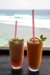 Two glasses with straws of fruit cocktails on the background of the Indian Ocean