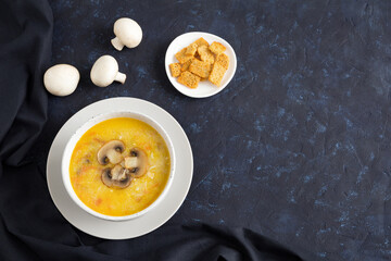Champignon soup in a white bowl on dark textile. Top of the soup is decorated with slices of sliced mushroom. Flat lay with place for text on dark blue background.