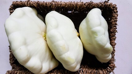 Three large white squash vegetables lying sideways in an open brown basket on a white background, close-up shot