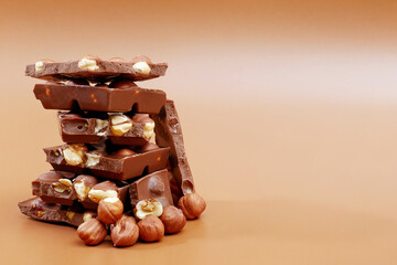 stack of milk chocolate pieces and hazelnuts on brown background
