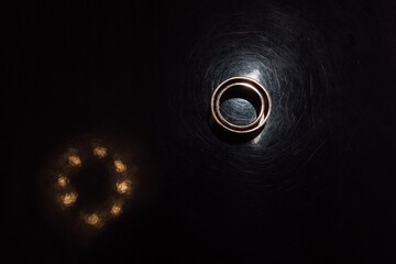 A gold ring lies on a black mirrored table with light reflection