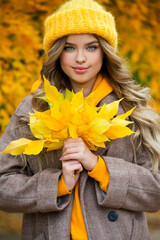 Beautiful girl walking outdoors in autumn. Smiling girl collects yellow leaves in autumn. Young woman enjoying autumn weather.