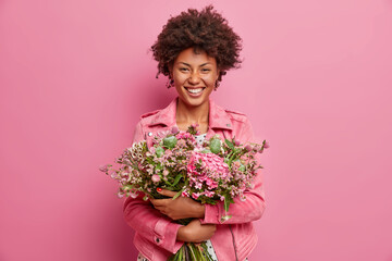 Horizontal shot of pretty African American woman expresses sincere emotions, embraces bouquet of...