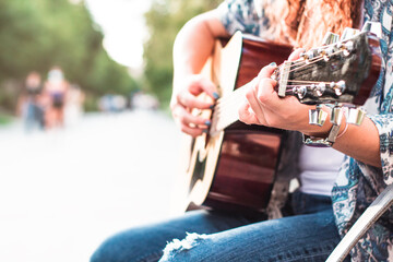 Beautiful woman playing a guitar sitting on a street bench. Selective focus.
