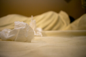 Fototapeta na wymiar A Young Man in a White Shirt Lying Sick in Bed With Tissues