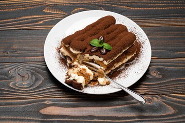 portion of Classic tiramisu dessert on ceramic plate on wooden background