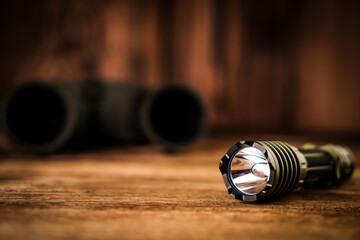 Detail close up of army - hunting binocular and flashlight on a blurred wooden background. 