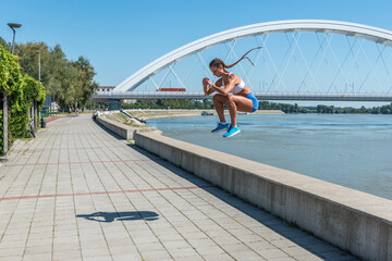 Young sexy strong fit woman in shorts jump with high knees as outdoor hardcore cardio cross workout training