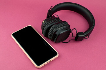 Smartphone and wireless black headphones. On-ear wireless headphones and the phone on a pink background