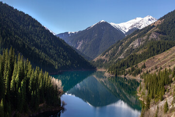 Fototapeta na wymiar Alpine lake Kolsay in Kazakkhstan. Coniferous forest-covered mountain slopes are reflected in the water.