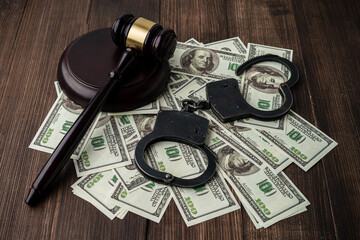 Judge's gavel with handcuffs on the background of dollar bills.