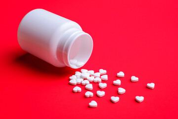 Small white pills fell from white plastic bottle to red background. Concept of heart treament, heart disease