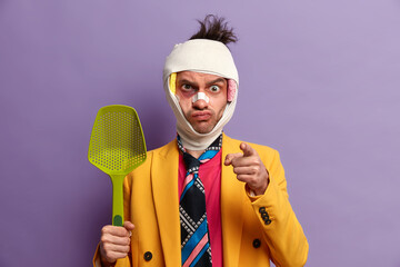 Angry serious adult man being injured, has brain concussion, wounded head, bruised skin, wears...