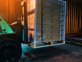 Worker driving forklift loading shipment carton boxes goods on wooden pallet at loading dock from container truck to warehouse cargo storage in freight logistics, transportation industrial, delivery