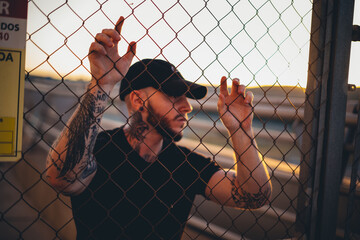 chico moda gorra reja urbano callejero de negro serio puesta de sol industrial moderno joven barba