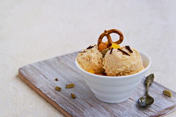 Dessert, homemade ice cream or frozen yogurt with persimmons, decorated with salted pretzels and grated chocolate, in a white bowl on a light concrete background.
