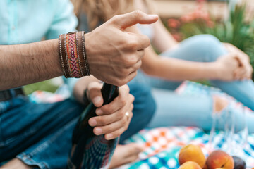 Close up man hands opening a sparkling wine while sitting on a blanket with his wife celebrating life, enjoying each other