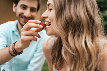 Smiling man feeding his young happy wife with strawberry. Cheerful couple with beautiful smiles