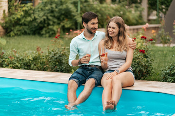 Summer holidays, people, romance, dating concept, couple drinking sparkling wine while enjoying time together sitting at the pool