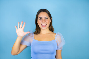 Young beautiful woman over isolated blue background showing and pointing up with fingers number five while smiling confident and happy