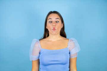 Young beautiful woman over isolated blue background making fish face with lips, crazy and comical gesture.