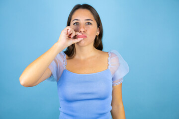 Young beautiful woman over isolated blue background mouth and lips shut as zip with fingers. Secret...