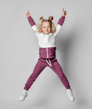 Cheerful baby girl in a stylish modern pink gray sports hoodie and pants jumps high.
