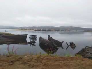 Fototapeta na wymiar Destroyed abandoned old wooden fishing ships on the shore of the Barents sea