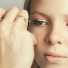make-up artist makes makeup of the model with false eyelashes. tweezers in the hand of the master. model preparation