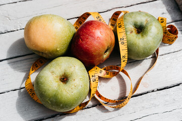 Delicious and healthy food is on the kitchen table. Four apples-yellow, green and red on a white wooden background and a yellow flexible centimeter ribbon.