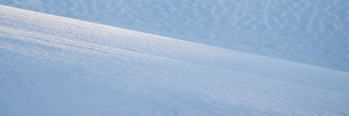 Obraz premium Beautiful winter background with snowy ground. Natural snow texture. Wind sculpted patterns on snow surface. Wide panoramic texture for background and design. Closeup top view with copy space.