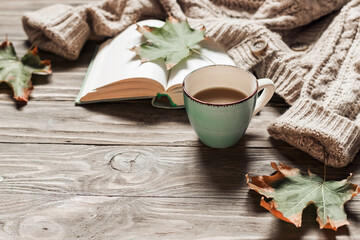 Autumn morning coffee. A cup of coffee on a wooden table and a warm sweater on a background of autumn leaves. Still life concept. Copy space.