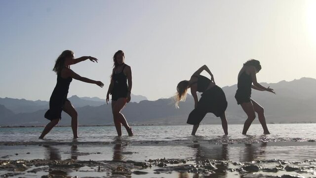 group of attractive females dancing ecstatic in sea at sunset slow motion
