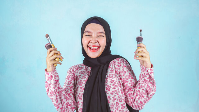 Closeup portrait of beautiful happy young hijab women with perfect skin is holding makeup brush in hand. 