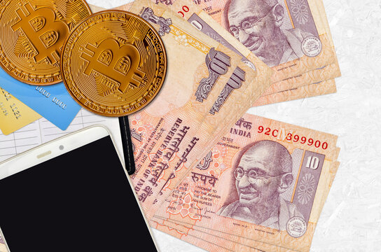 10 Indian rupees bills and golden bitcoins with smartphone and credit cards. Cryptocurrency investment concept. Crypto mining or trading