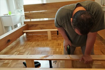 A man screwing screws in a wooden beams in assembling a new bed as improvement of his home. He is...