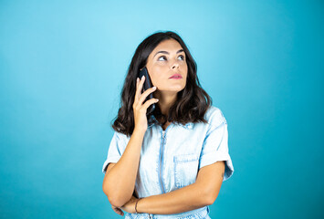 Young beautiful woman wearing a denim jumpsuit over isolated blue background talking with her phone.