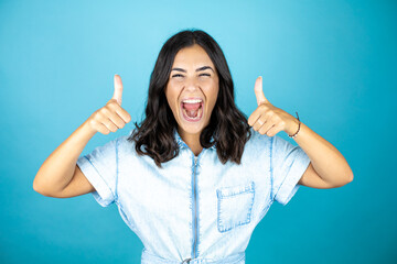 Young beautiful woman wearing a denim jumpsuit over isolated blue background smiling and doing the ok signal with thumbs.