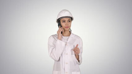 Woman engineer talking on the phone while walking on gradient background.